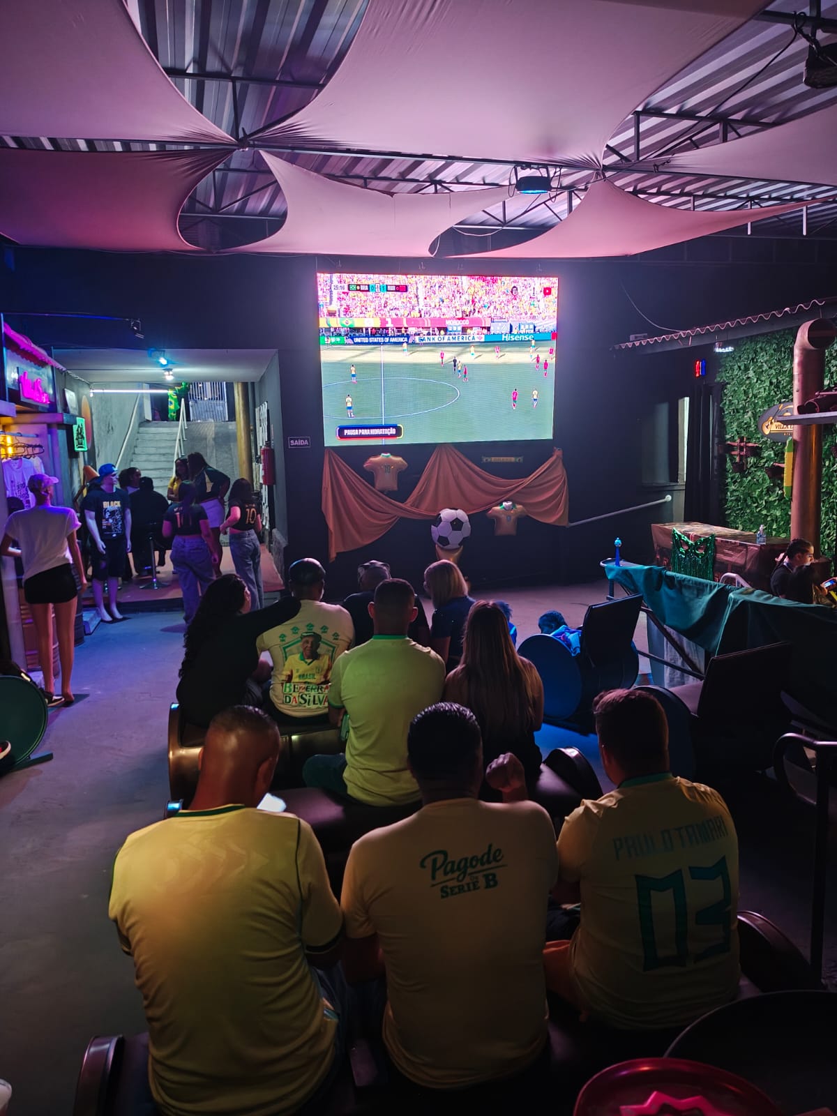 Grupo de amigos vestindo camisas do Brasil e da série Pagode Série B assistindo Copa do Mundo na Villa do Som
